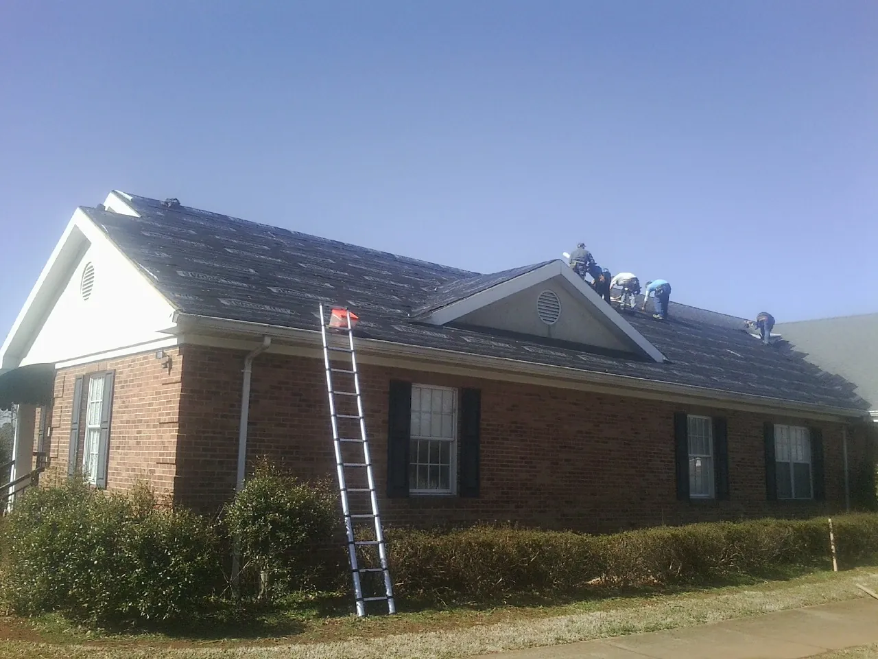 Crew tearing shingles off a brick ranch roof with a ladder set — Emergency Roof Repair work by our crew in Wade