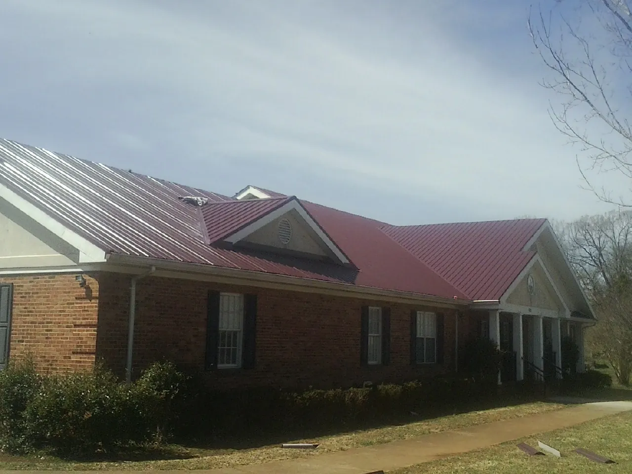 Red metal roof with gabled entries on a long brick building, from a Hail Damage Roof Repair job in Wade