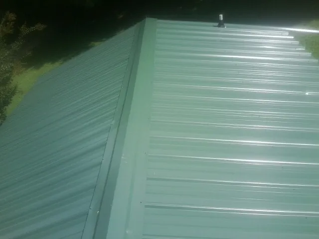 New green metal panels meeting at the ridge of a roof — Flat Roof Repair work by our crew in Wade