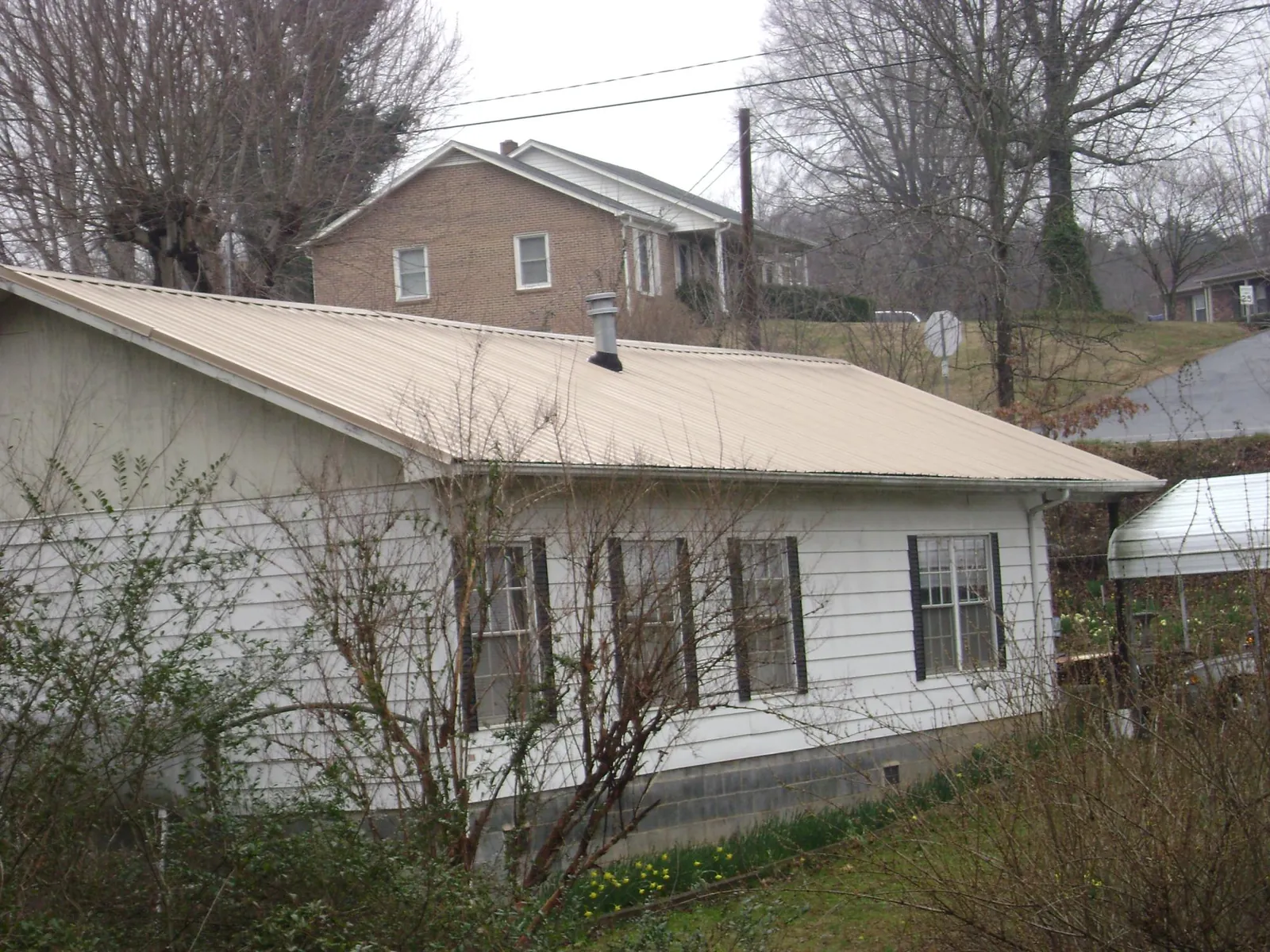 Tan metal roof on a white sided house set into a hillside — Commercial Roofing by Roofing Brothers in Wade